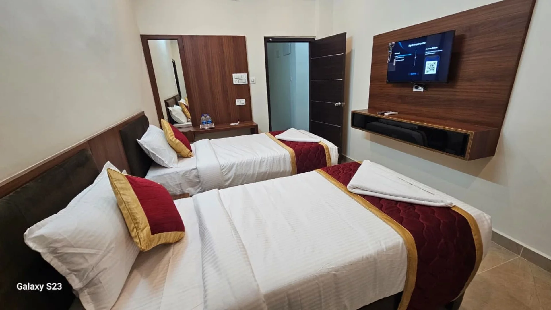 Twin-bed guest room with a wall-mounted television and dressing mirror