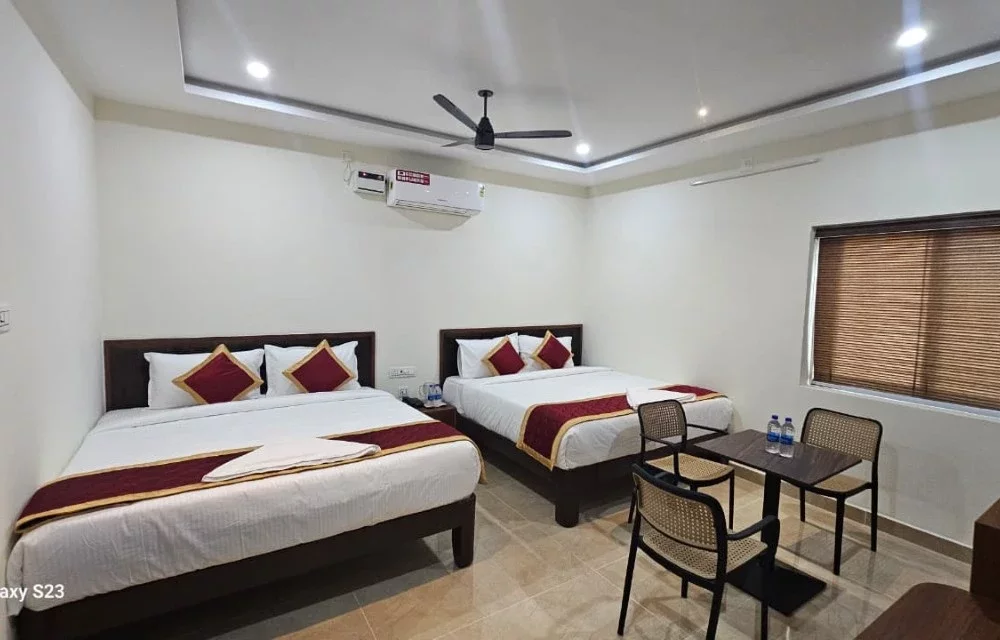 Wide view of a larger guest room with two double beds and seating